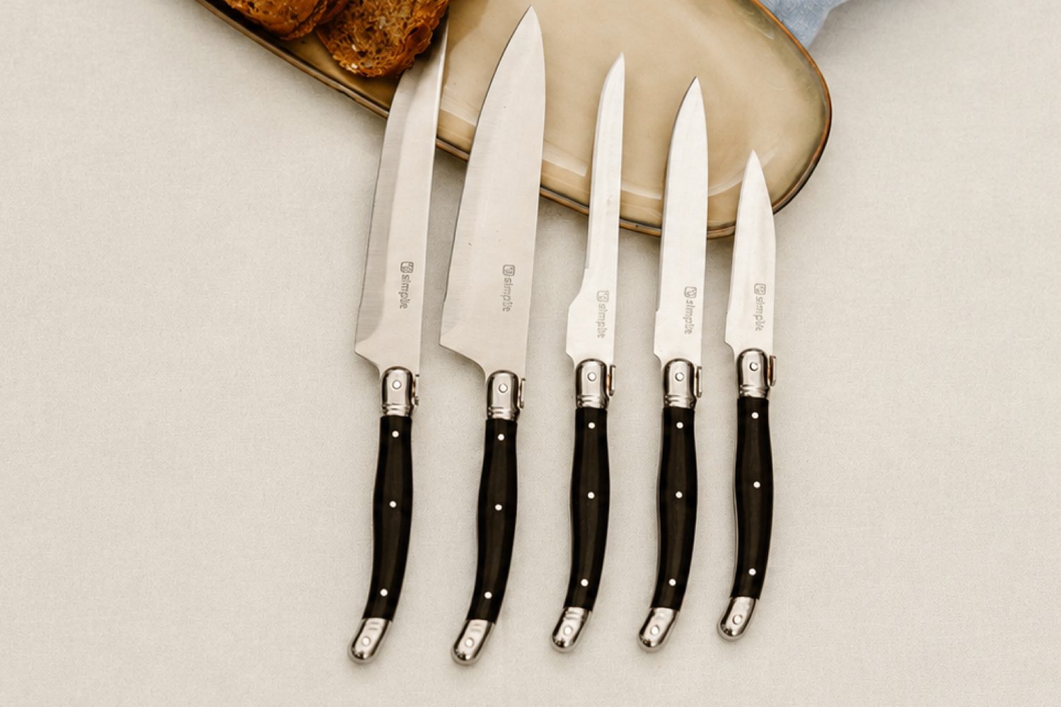 Simplit Set Cuchillos Paris — lay flat 5 cuchillos acero inoxidable mango negro sobre fondo crema